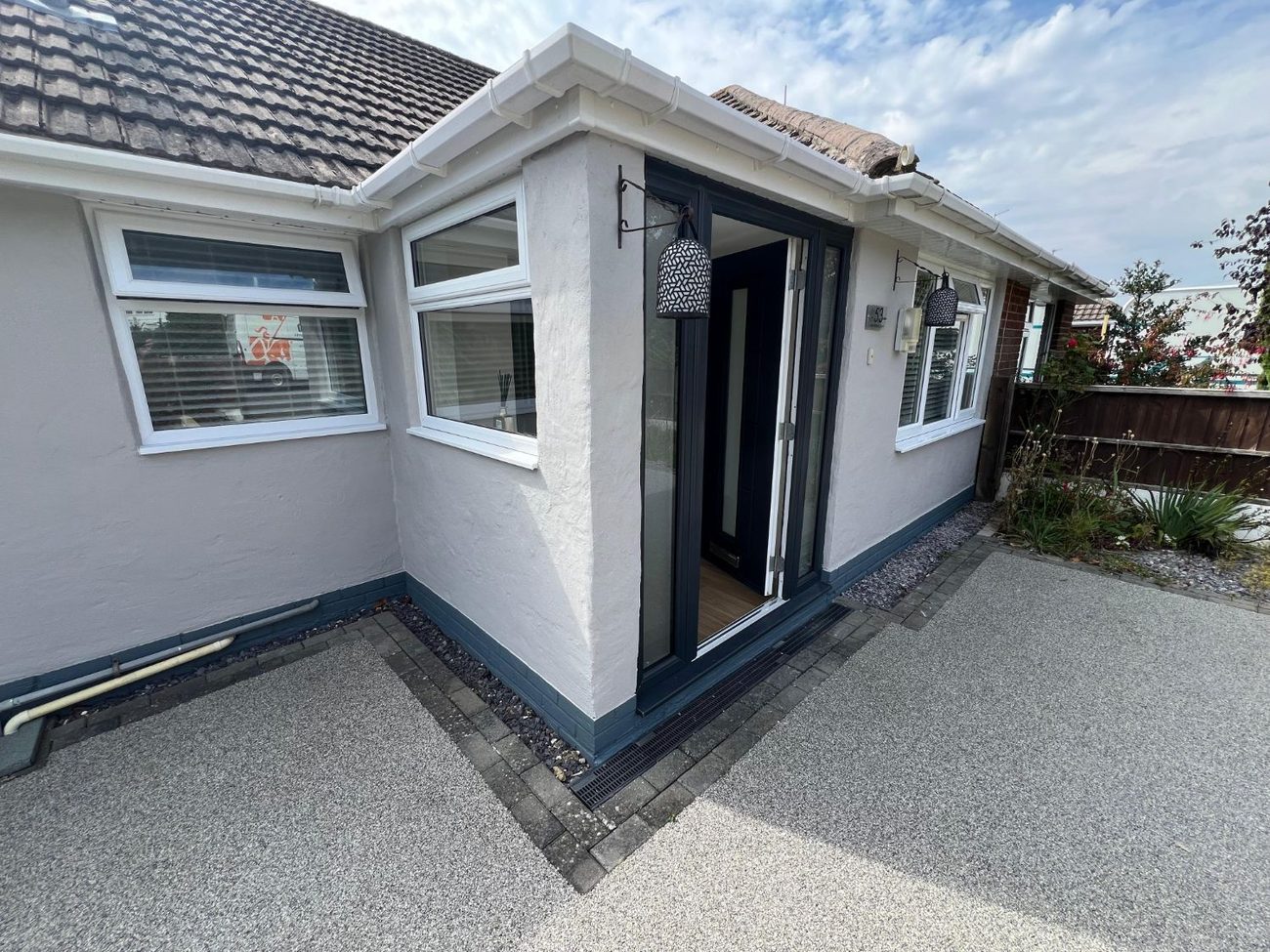 A bungalow with freshly painted exterior walls, a dark blue plinth and a new resin drive