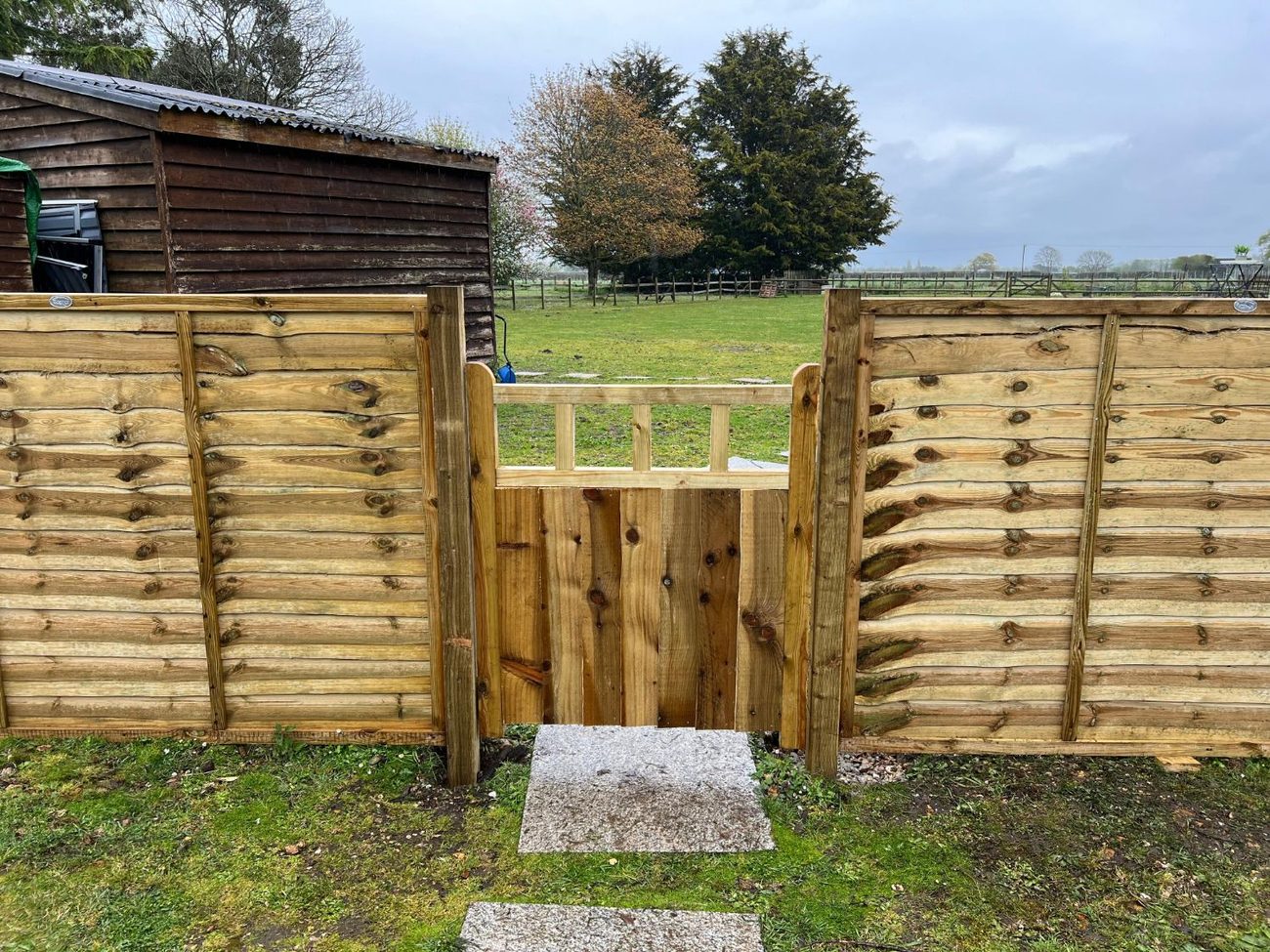 A new wooden gate set between two sections of wooden panel fencing