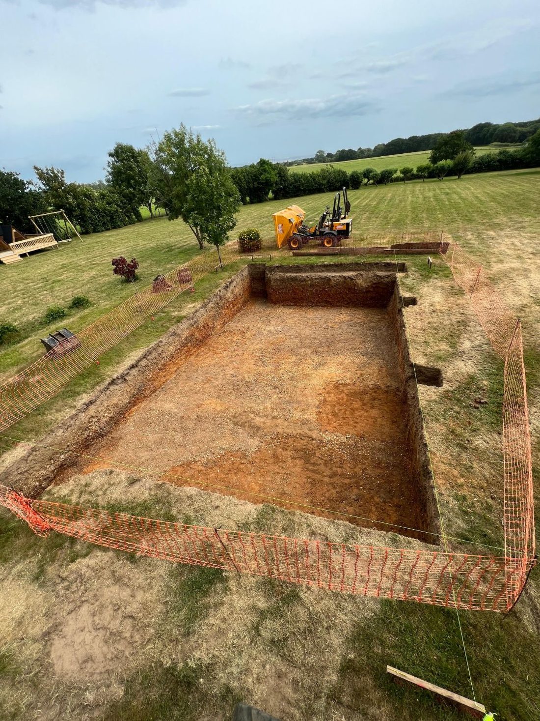 A large rectangular excavation in a garden, fenced off, ready for a swimming pool